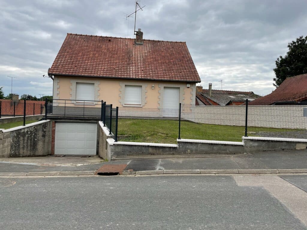 Vue extérieure du pavillon à Saint Léger les Domart avec toit en tuiles rouges, jardin clôturé et garage en sous-sol