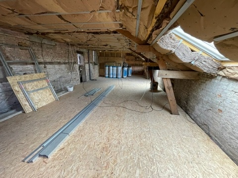 Combles en cours de rénovation dans une grange de la Somme avec plancher posé et ouvertures pour les fenêtres de toit