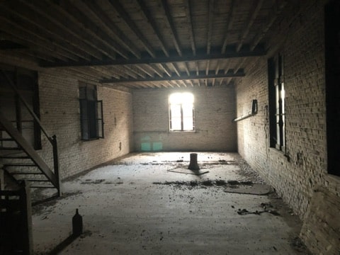 Intérieur d'une grange en brique dans la Somme avant sa transformation en logements, avec fenêtres et poutres apparentes.