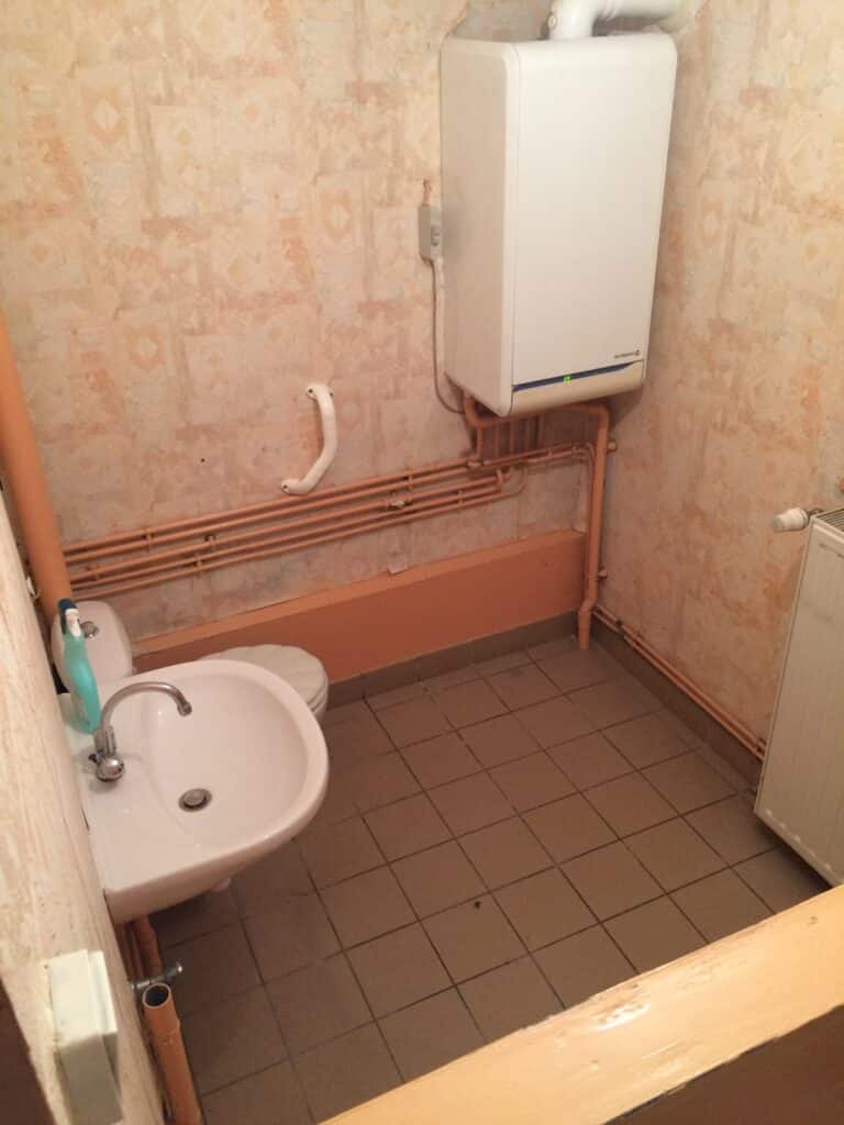 Salle de bain délabrée de la maison de ville à Moreuil avec lavabo, WC et chaudière murale.